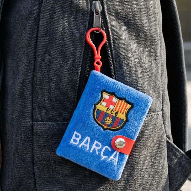 Minilibreta de peluche del FC Barcelona colgada del enganche rojo en una mochila escolar negra.