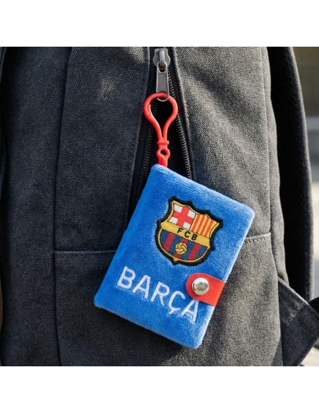 Minilibreta de peluche del FC Barcelona colgada del enganche rojo en una mochila escolar negra.