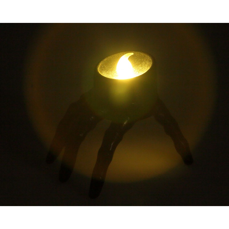 Vela LED con forma de mano de Halloween encendida en la oscuridad mostrando la luz superior cálida.